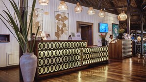 A reception area with a wooden reception desk, a large potted plant, and hanging wicker lamps. - Vanila Hotel & Spa (Nosy Be)