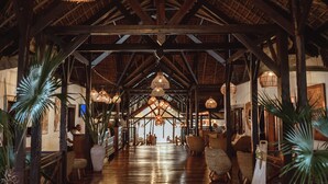 A spacious corridor with high ceilings and wooden beams, lined with wicker furniture and hanging wicker lamps. - Vanila Hotel & Spa (Nosy Be)