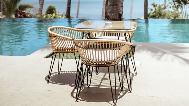 A poolside area with wicker chairs and a glass table, surrounded by palm trees and a view of the ocean. - Vanila Hotel & Spa (Nosy Be)