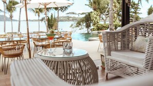 An outdoor seating area with wicker furniture, a glass table, and a view of the sea. - Vanila Hotel & Spa (Nosy Be)