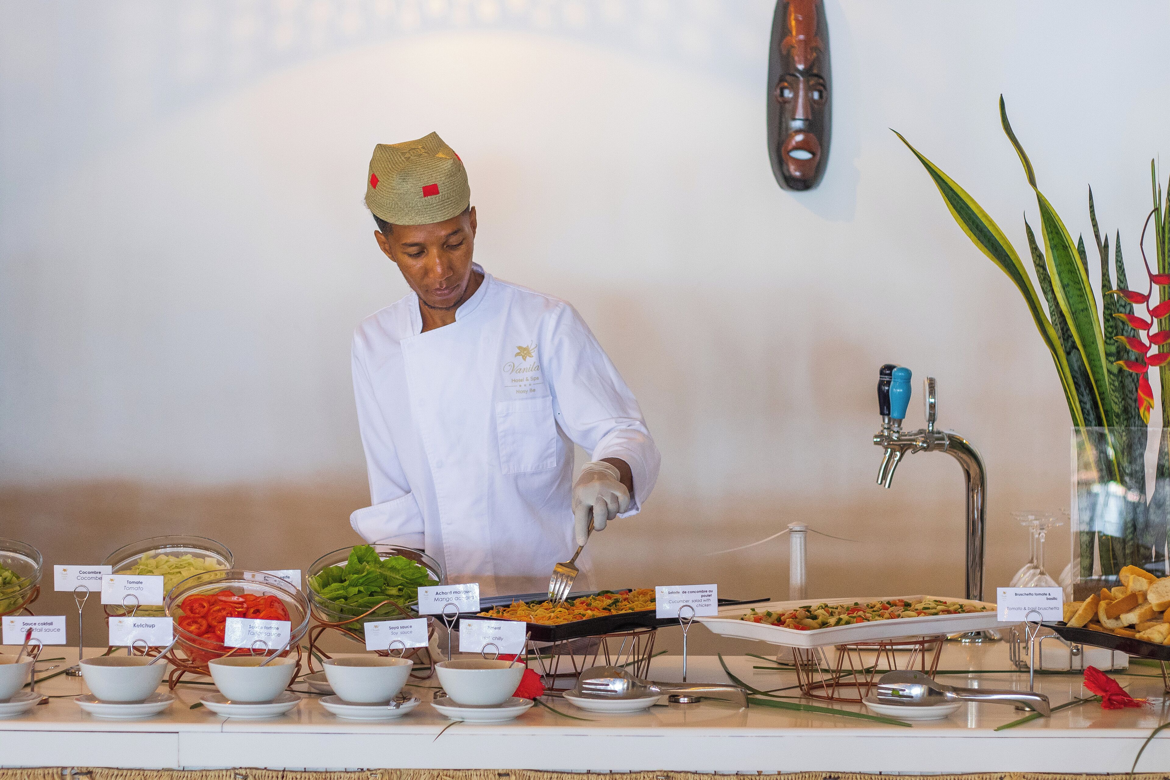 A buffet setup with various food items and a server in a white uniform.