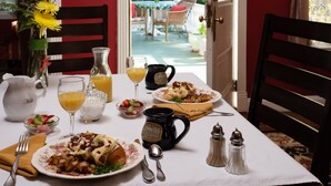 Una mesa de desayuno dispuesta con platos de comida, una jarra, un vaso de jugo de naranja, una taza de café y saleros y pimenteros.