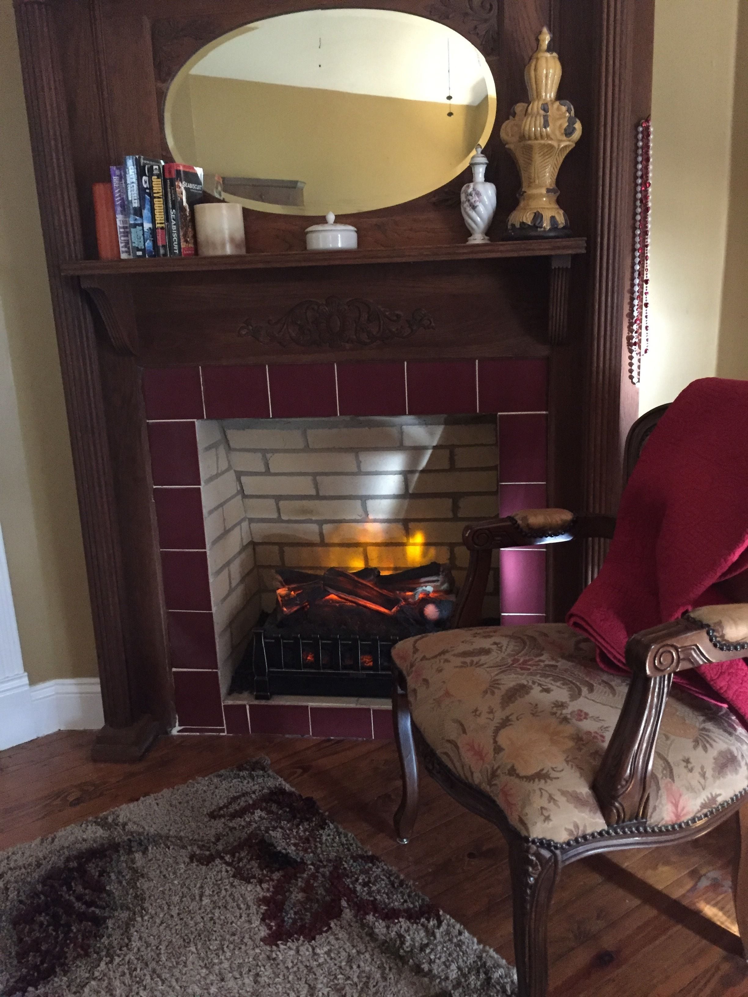 A fireplace with a brick surround, a mirror above it, and a chair with a floral pattern.