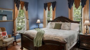 Un dormitorio con una cama grande, una silla, una mesita de noche y una ventana con cortinas.