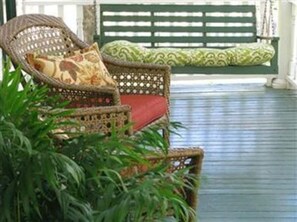 Una silla de mimbre con un cojín rojo y una almohada estampada, ubicada frente a un banco verde con un cojín a juego.