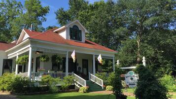 A white colonial-style building with a red roof, a porch with hanging plants, and a sign indicating it is a bed and breakfast.