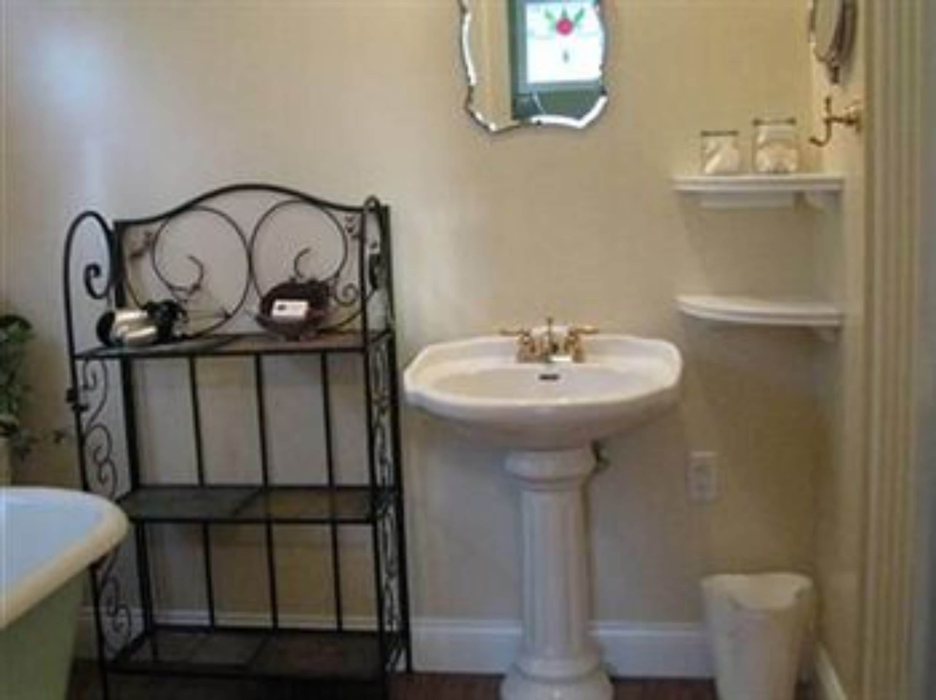 Un bagno con un lavabo su piedistallo, un piccolo ripiano con articoli da toilette e un ripiano decorativo in metallo.