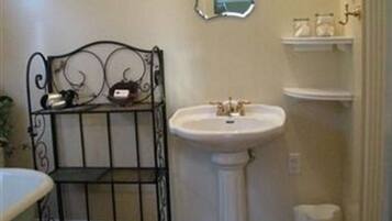 Un bagno con un lavabo su piedistallo, un piccolo ripiano con articoli da toilette e un ripiano decorativo in metallo.