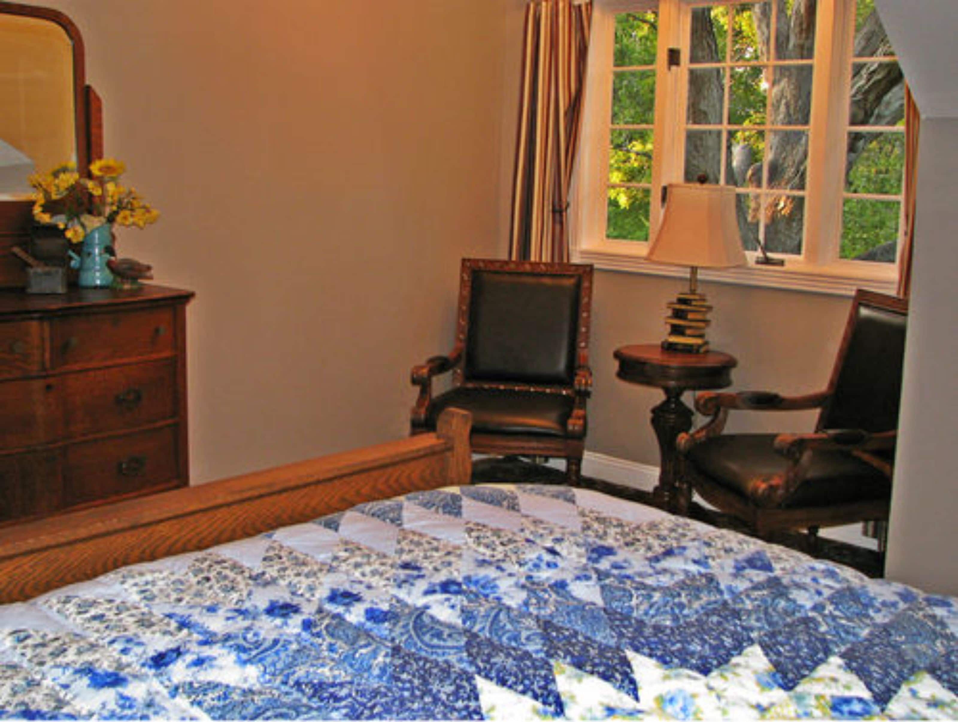 A bedroom with a bed, two chairs, a dresser, a lamp, and a window with curtains.