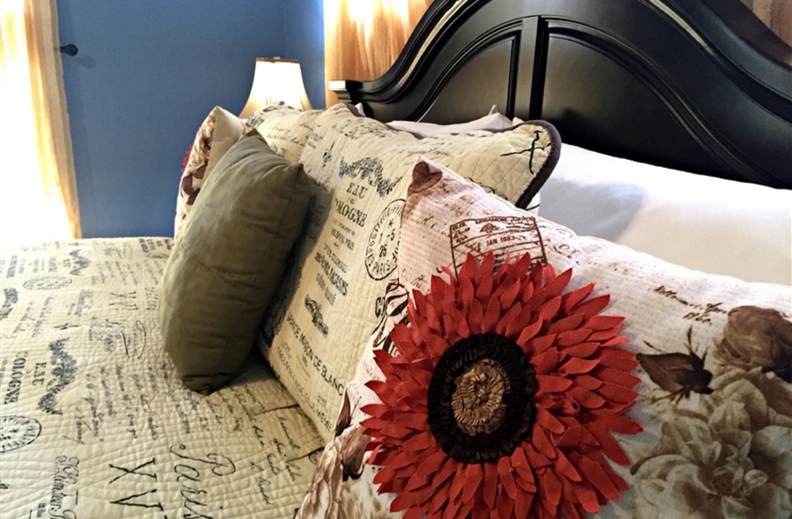 A bed with a floral-patterned bedspread and a red flower decoration, a pillow, and a black headboard.