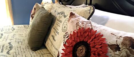 A bed with a floral-patterned bedspread and a red flower decoration, a pillow, and a black headboard.