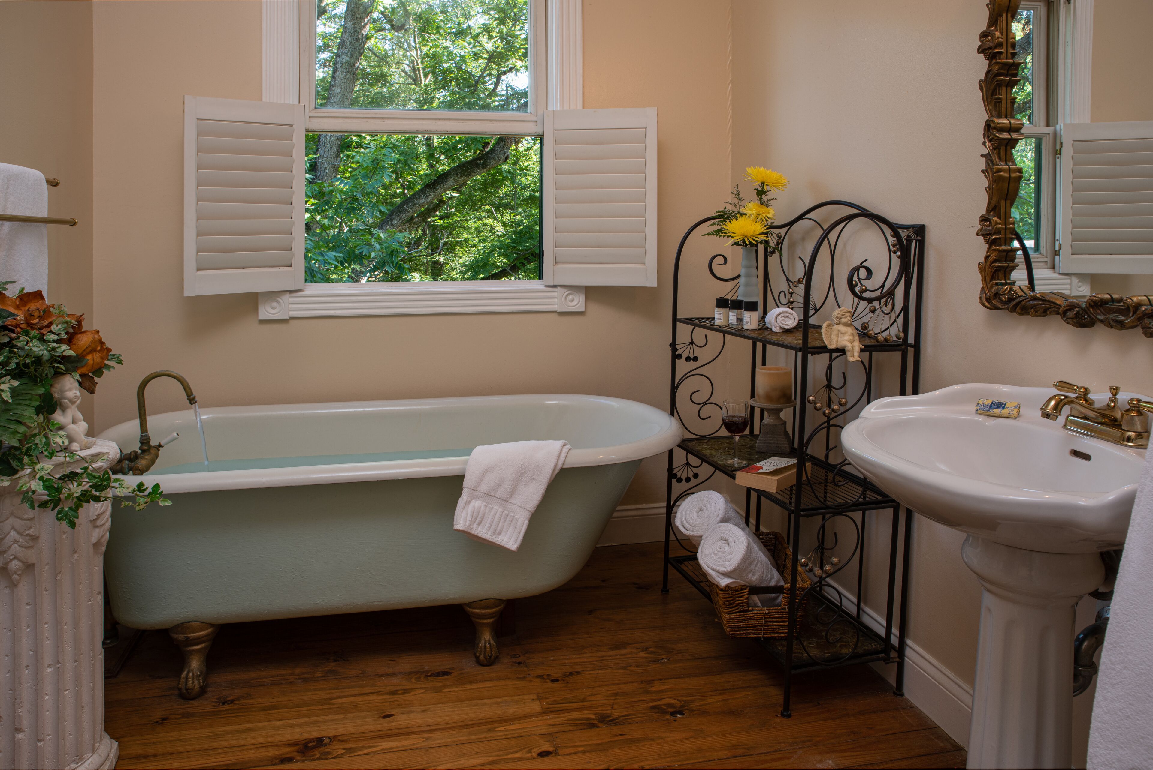 A bathroom with a freestanding bathtub, a sink, and a window with shutters.