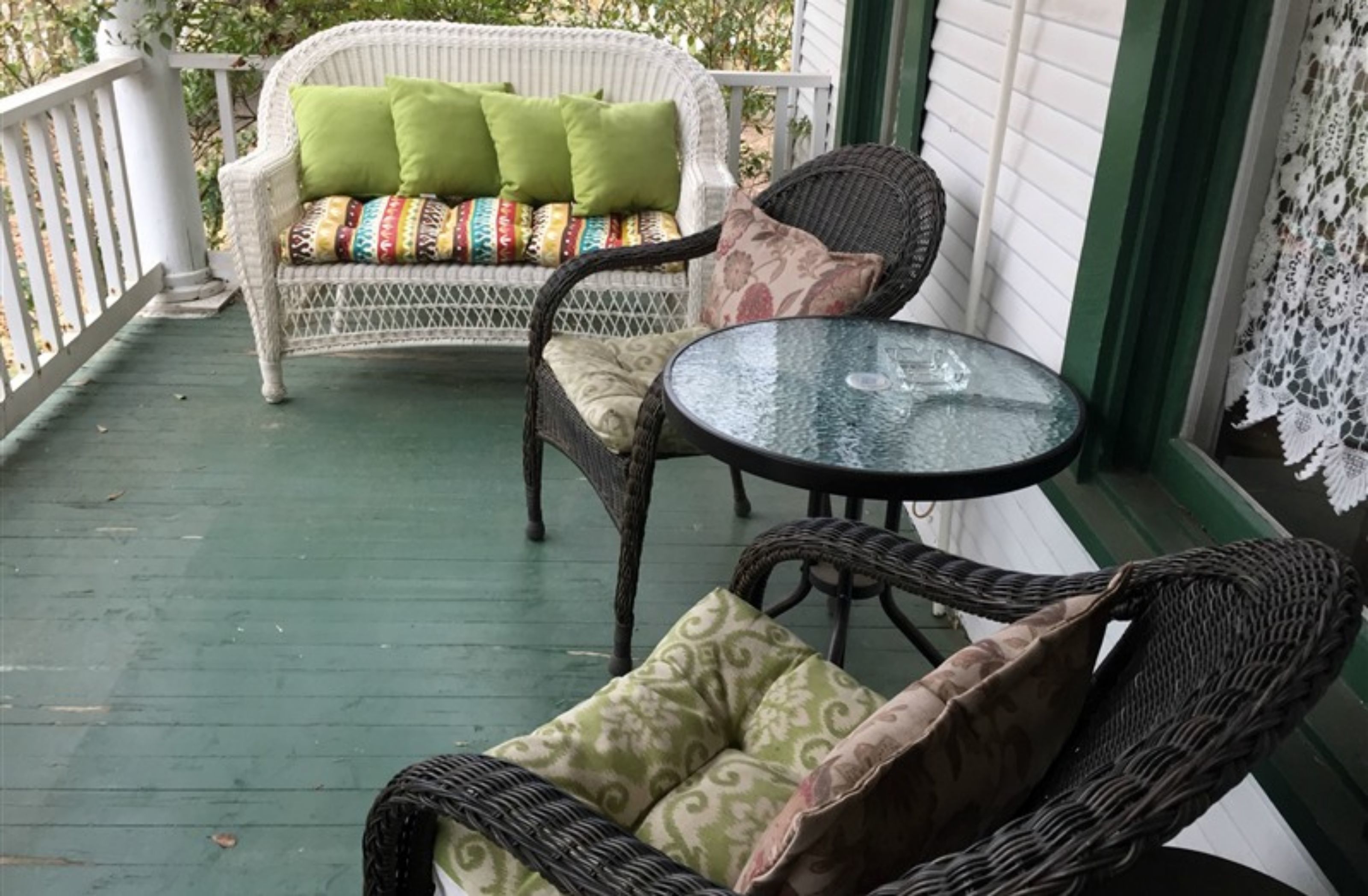 A porch with wicker furniture, a glass table, and a white sofa with colorful cushions.