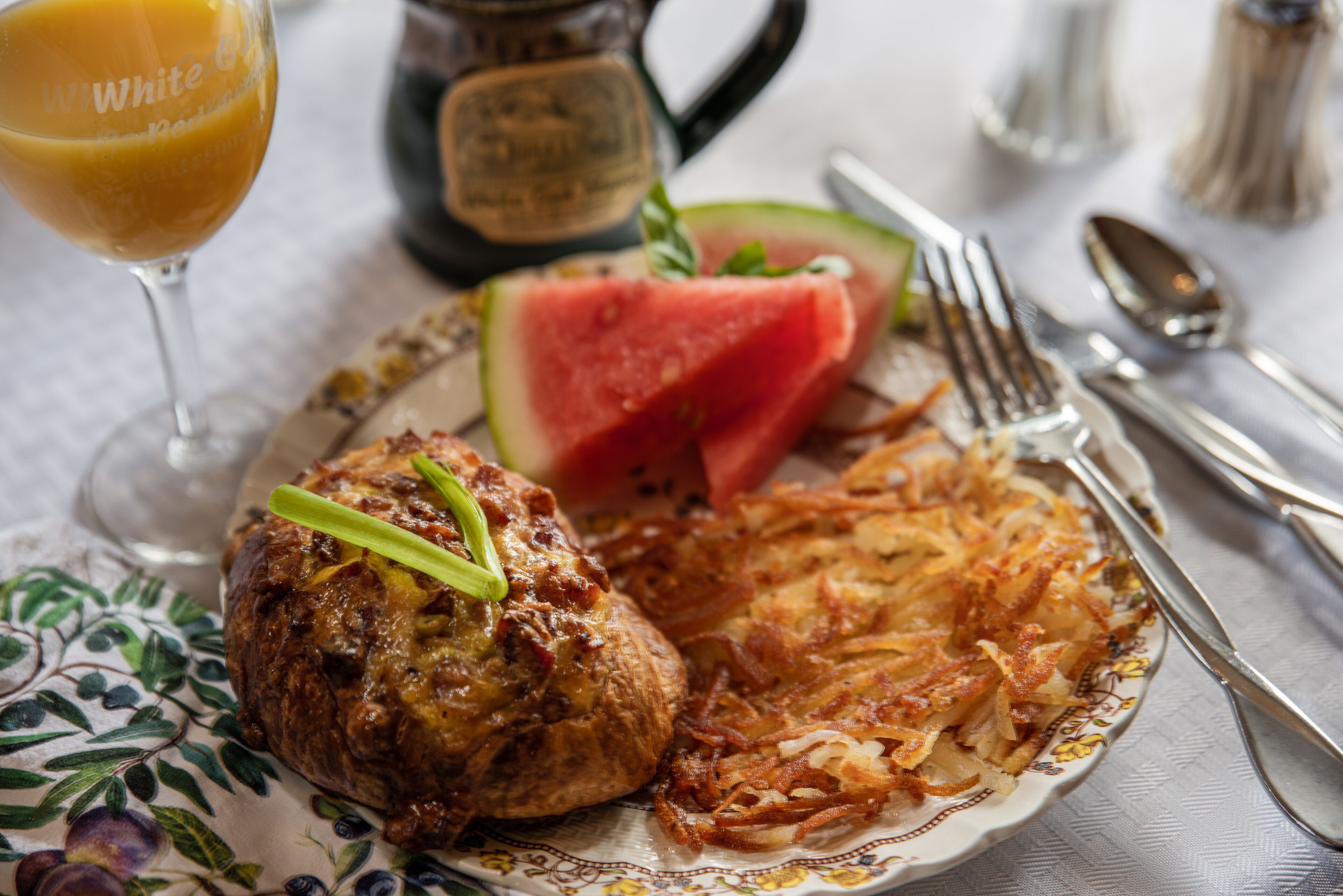 A plate with food including a meatball, hash browns, and a slice of watermelon.