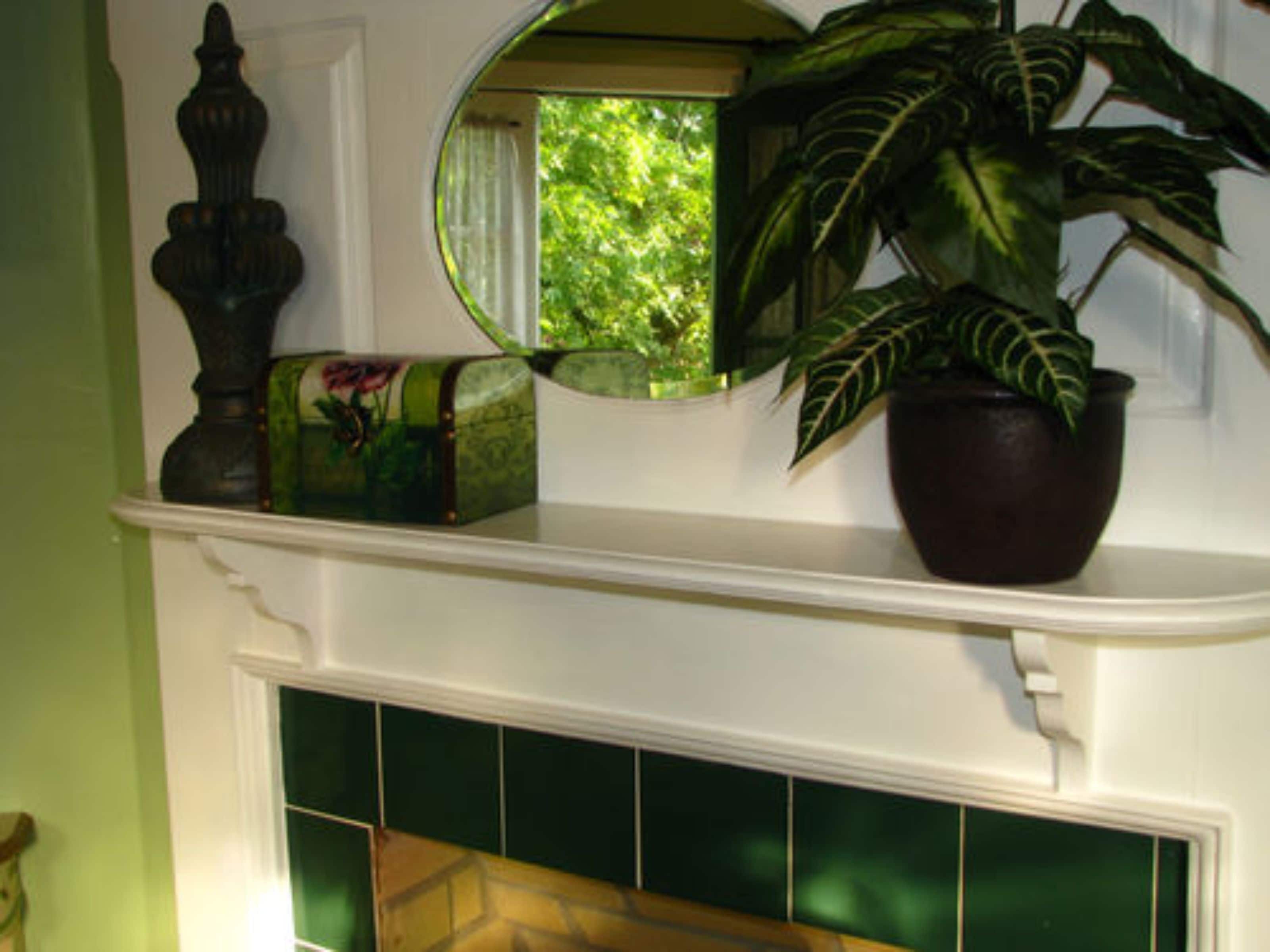 Une cheminée ornée de carreaux verts, une plante en pot, un miroir et une boîte décorative.