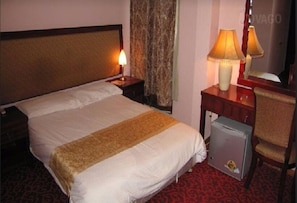 A hotel room with a bed, two bedside lamps, a small refrigerator, and a chair.