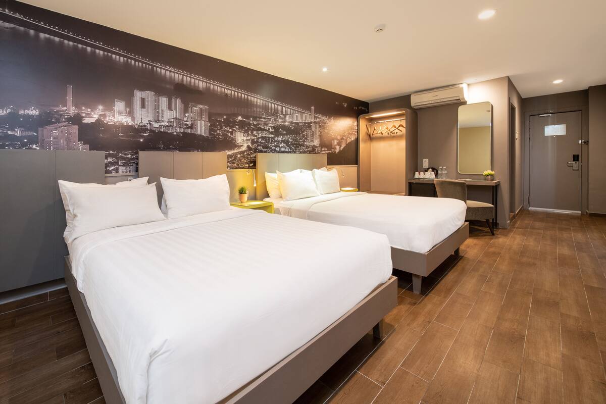 Une chambre d’hôtel avec deux lits, une fresque représentant un paysage urbain, une coiffeuse avec un miroir et un plancher en bois.
