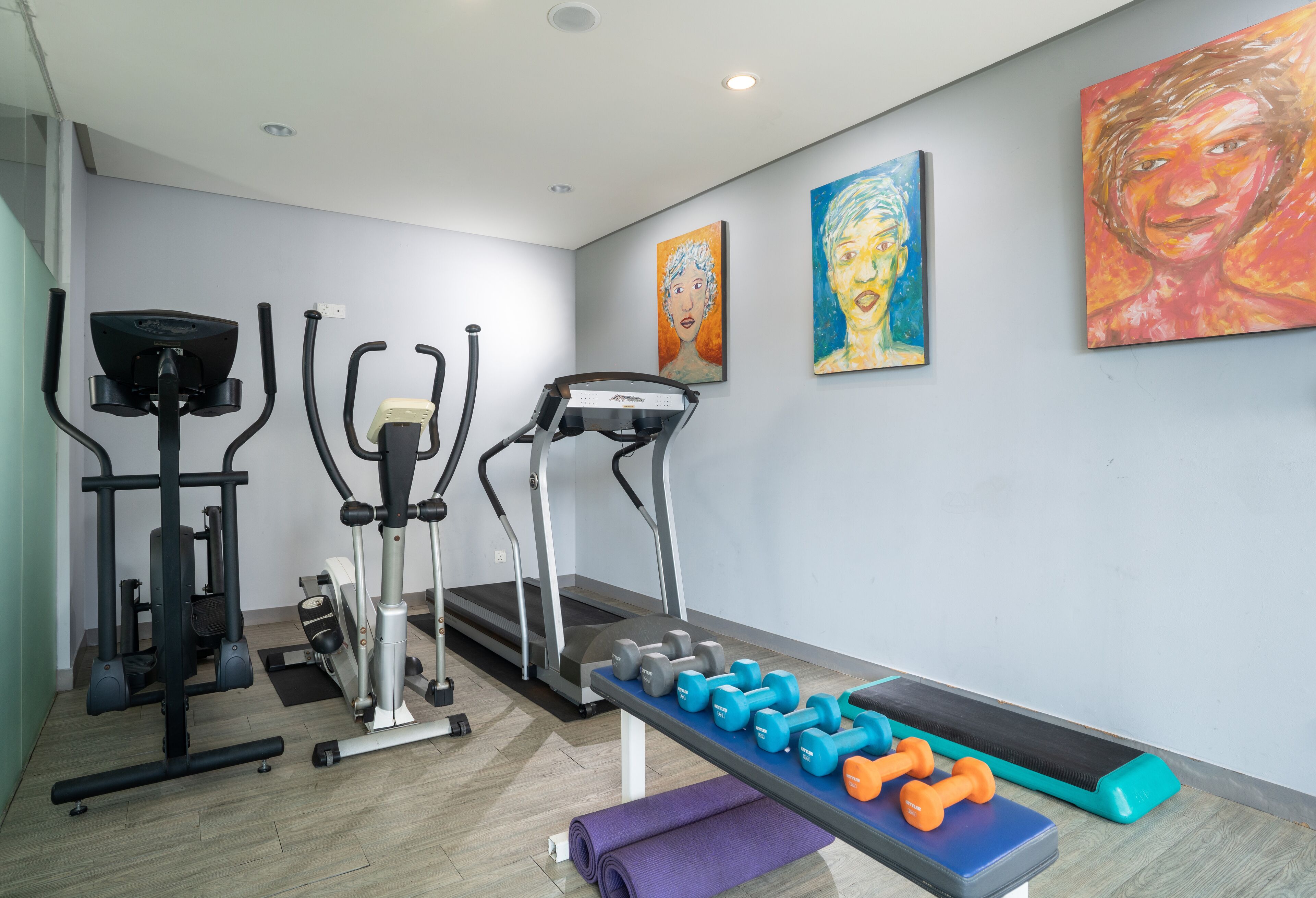 A gym with exercise equipment, including treadmills and dumbbells, and a bench.