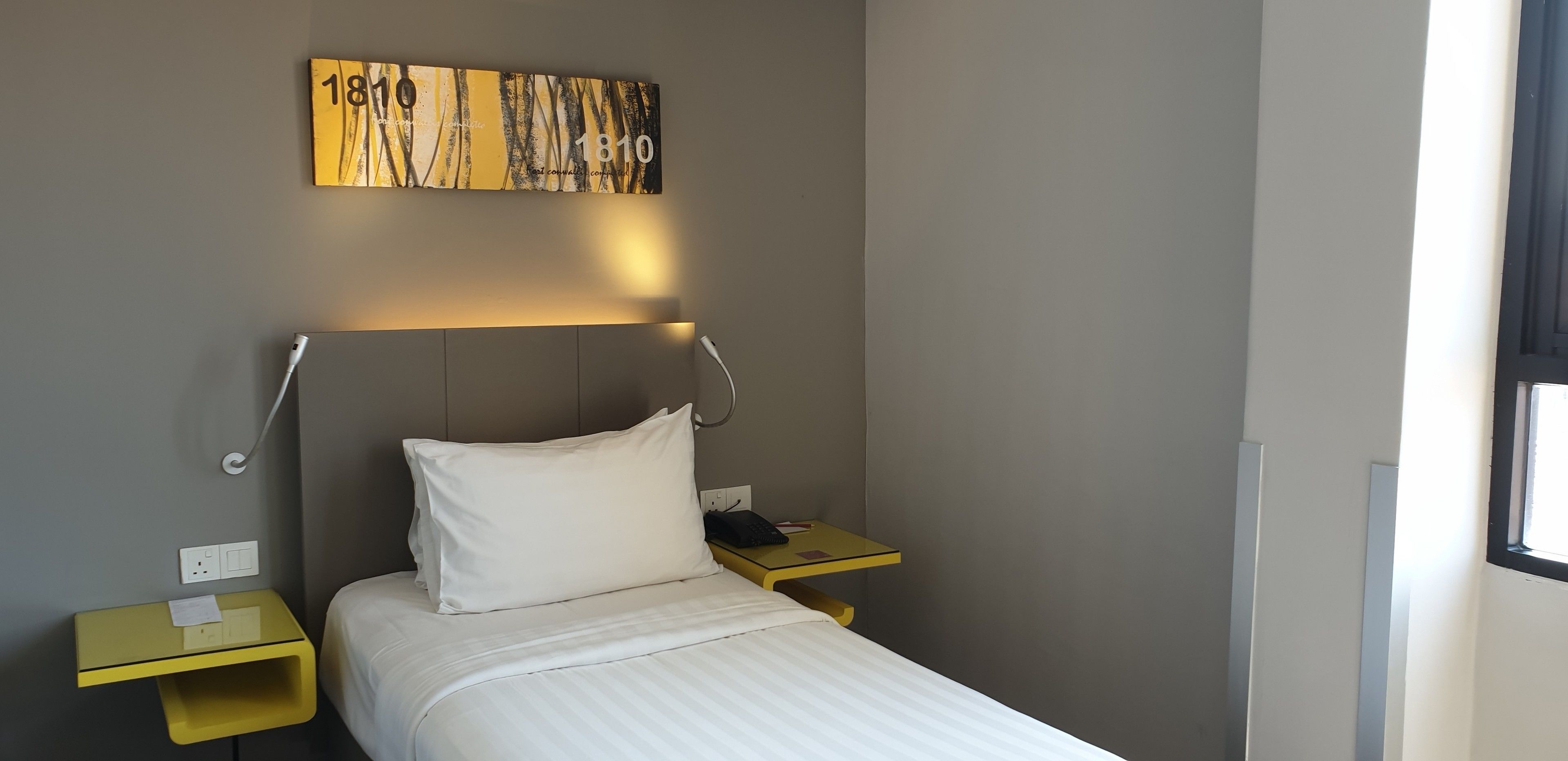 A hotel room with a bed, a nightstand, a bedside table, a wall-mounted artwork, and a window.