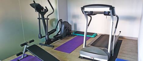 Un gimnasio con máquinas de cardio, una banca y colchonetas de ejercicio.