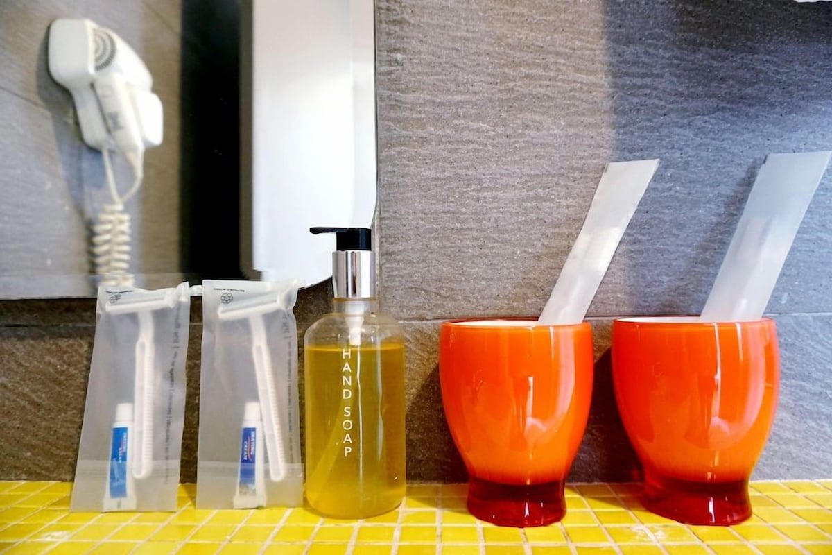 A bathroom counter with hand soap, a hairdryer, and two orange cups.