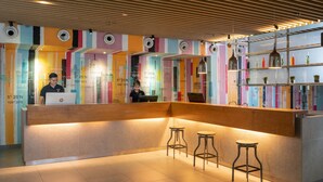 A reception area with a wooden counter, two bar stools, and a colorful wall with maps and text. - Travelodge Georgetown (George Town)