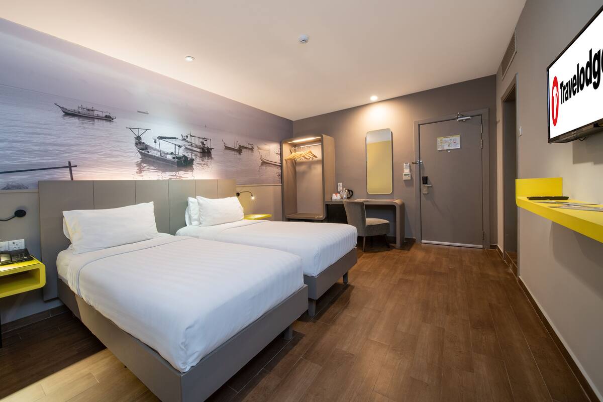 Une chambre d’hôtel moderne avec deux lits, un bureau, un miroir et une fresque murale représentant des bateaux.