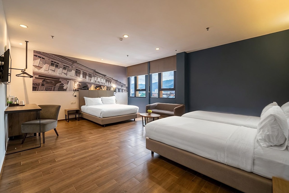 A modern hotel room with a large bed, a desk, a chair, and a sofa.