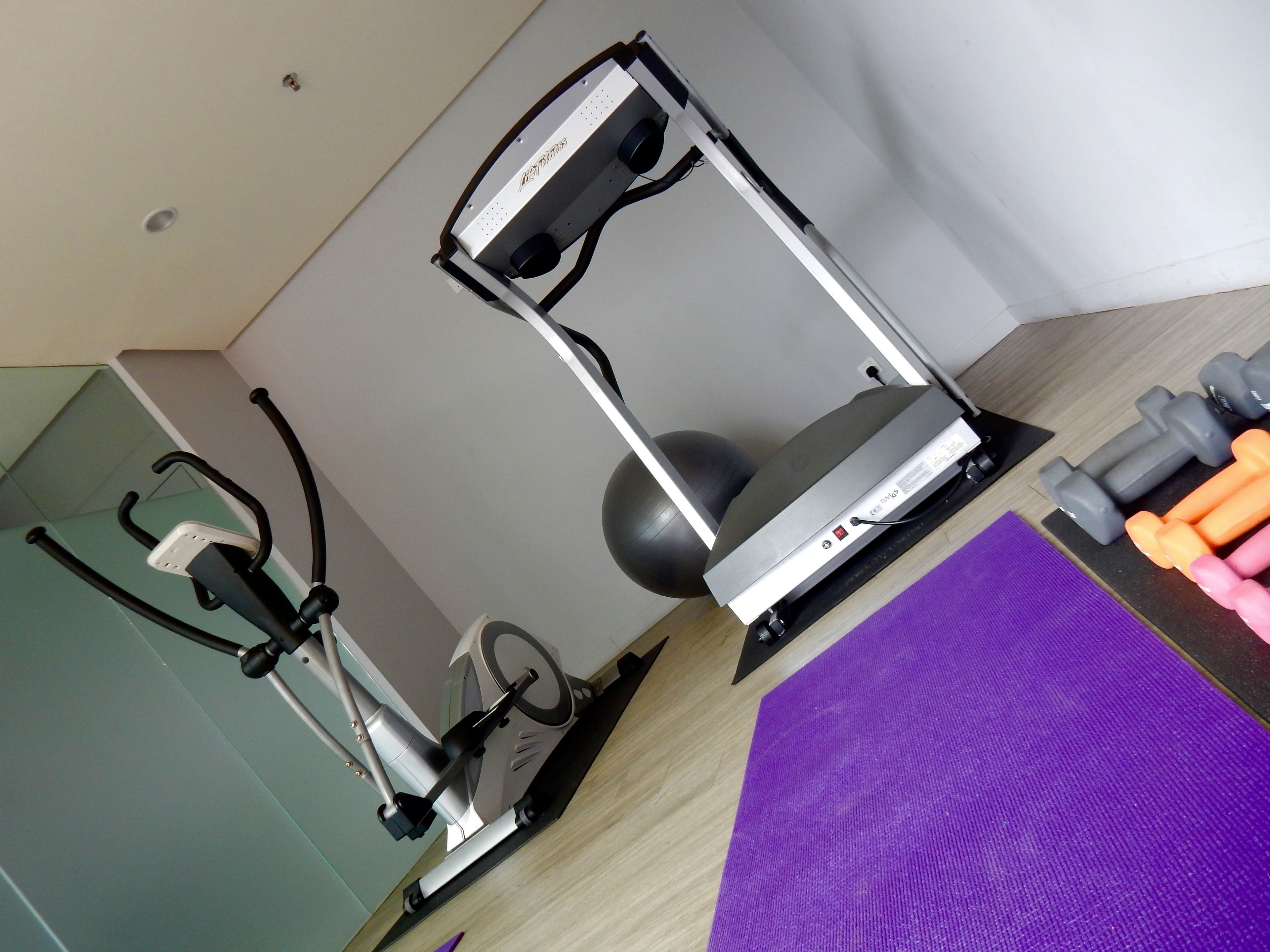 A home gym with a stationary bike, a treadmill, dumbbells, and a yoga mat.