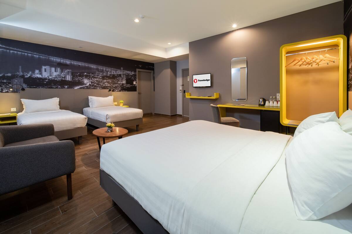 Une chambre d’hôtel moderne équipée d’un grand lit, de deux petits lits, d’un bureau et d’une chaise.