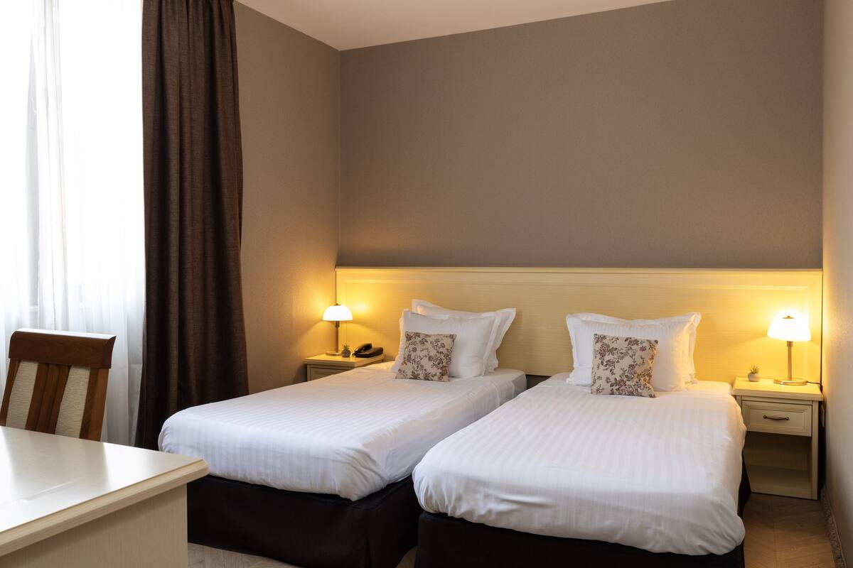 A hotel room with two single beds, a desk, and a chair.