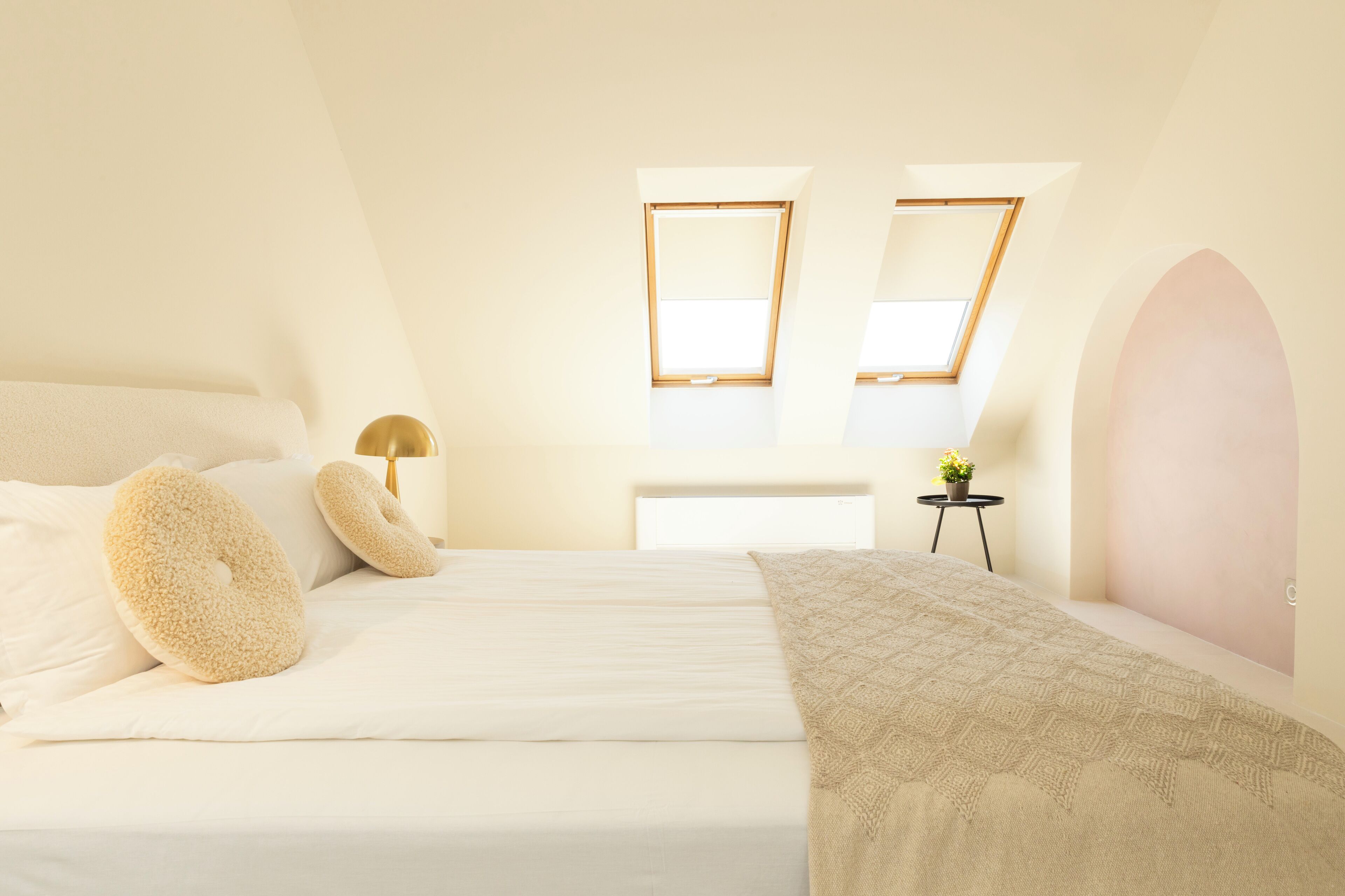 A bedroom with a bed, pillows, a bedside table with a lamp, and a window.
