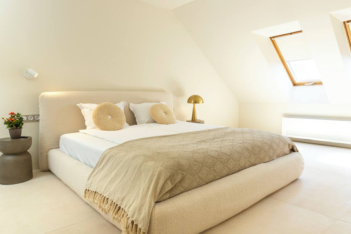 A modern bedroom with a large bed, a bedside table, a lamp, and a window.