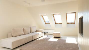Un salón moderno y minimalista con un amplio sofá en forma de L, una pequeña mesa redonda y un gran ventanal que proporciona luz natural.