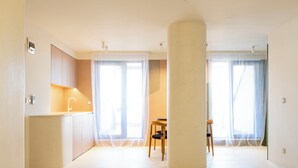 Amplia sala de estar con un gran pilar, una cocina con un lavabo y un comedor con una silla.
