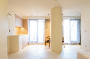 A spacious living area with a large column, a kitchen with a sink, and a dining area with a chair.