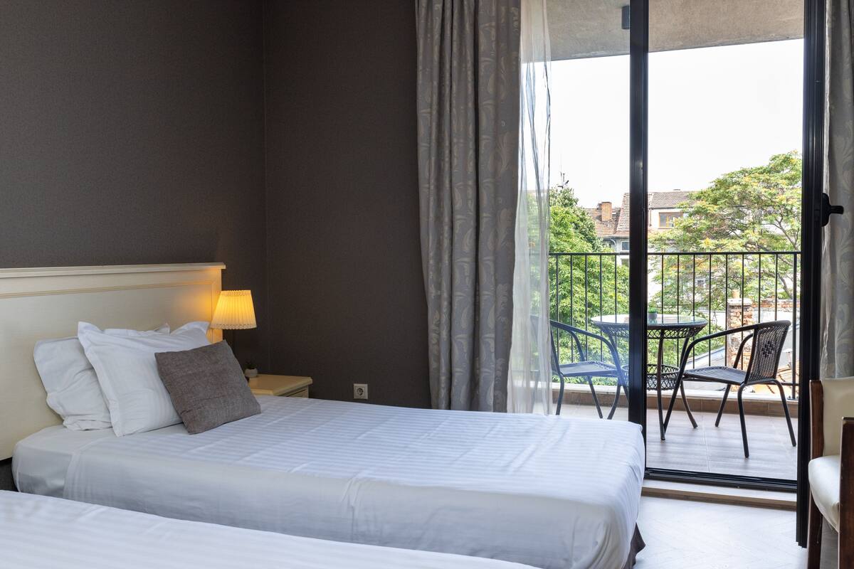 A hotel room with two beds, a balcony with a table and chairs, and a view of the city.