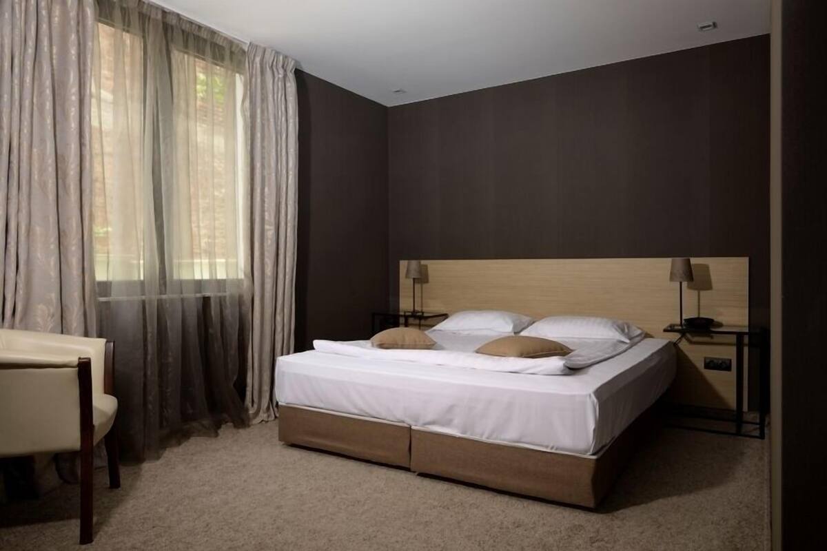 A neatly arranged bedroom with a bed, bedside tables, a chair, and a window with curtains.