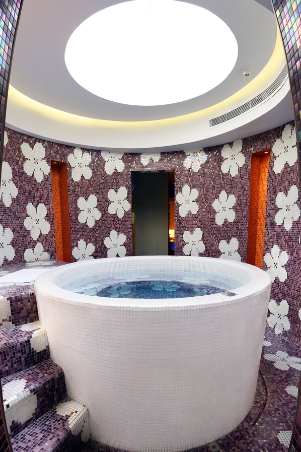 Relax in a serene hot tub surrounded by a mosaic-adorned wall and patterned design.