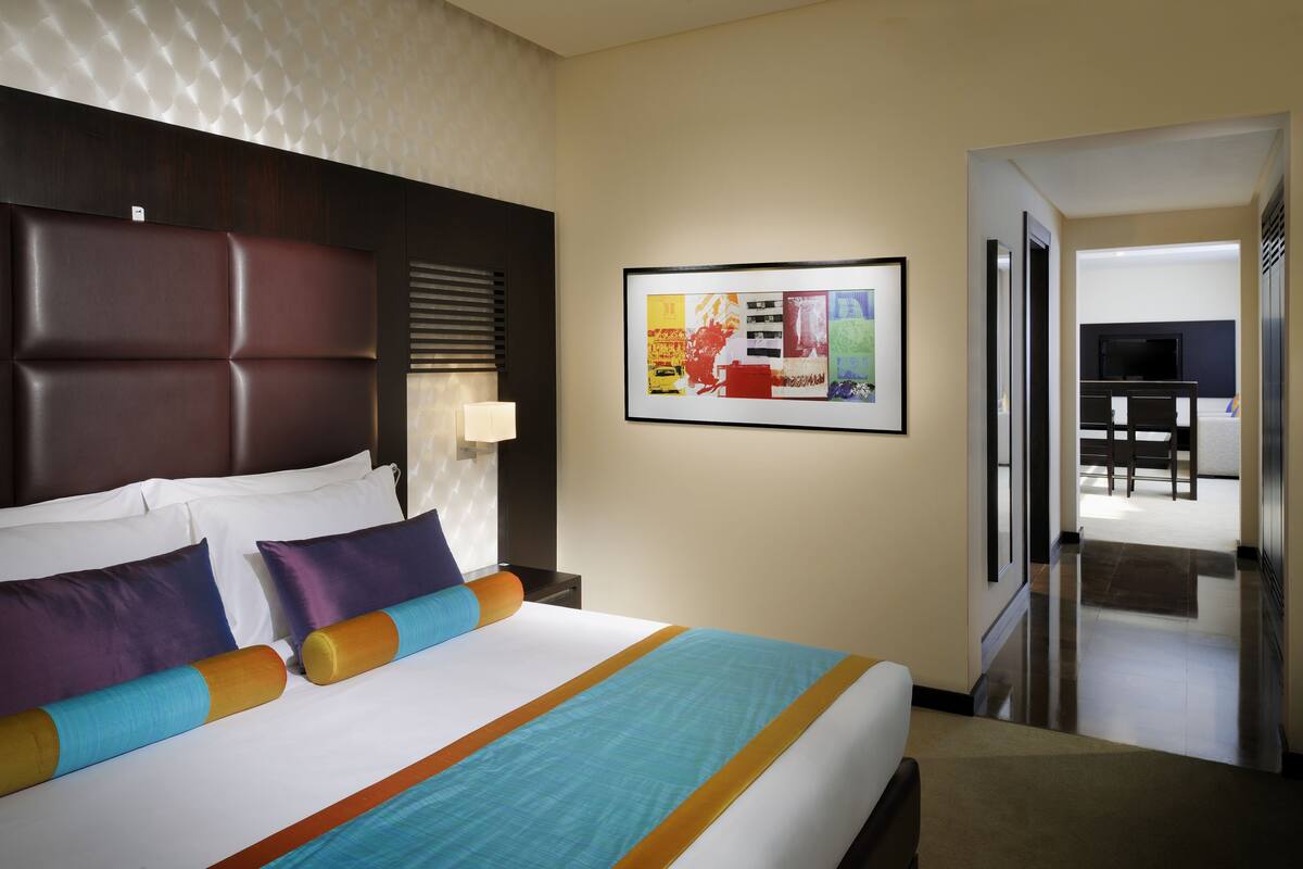 A hotel room with a large bed, a headboard, a wall-mounted TV, and a framed picture.