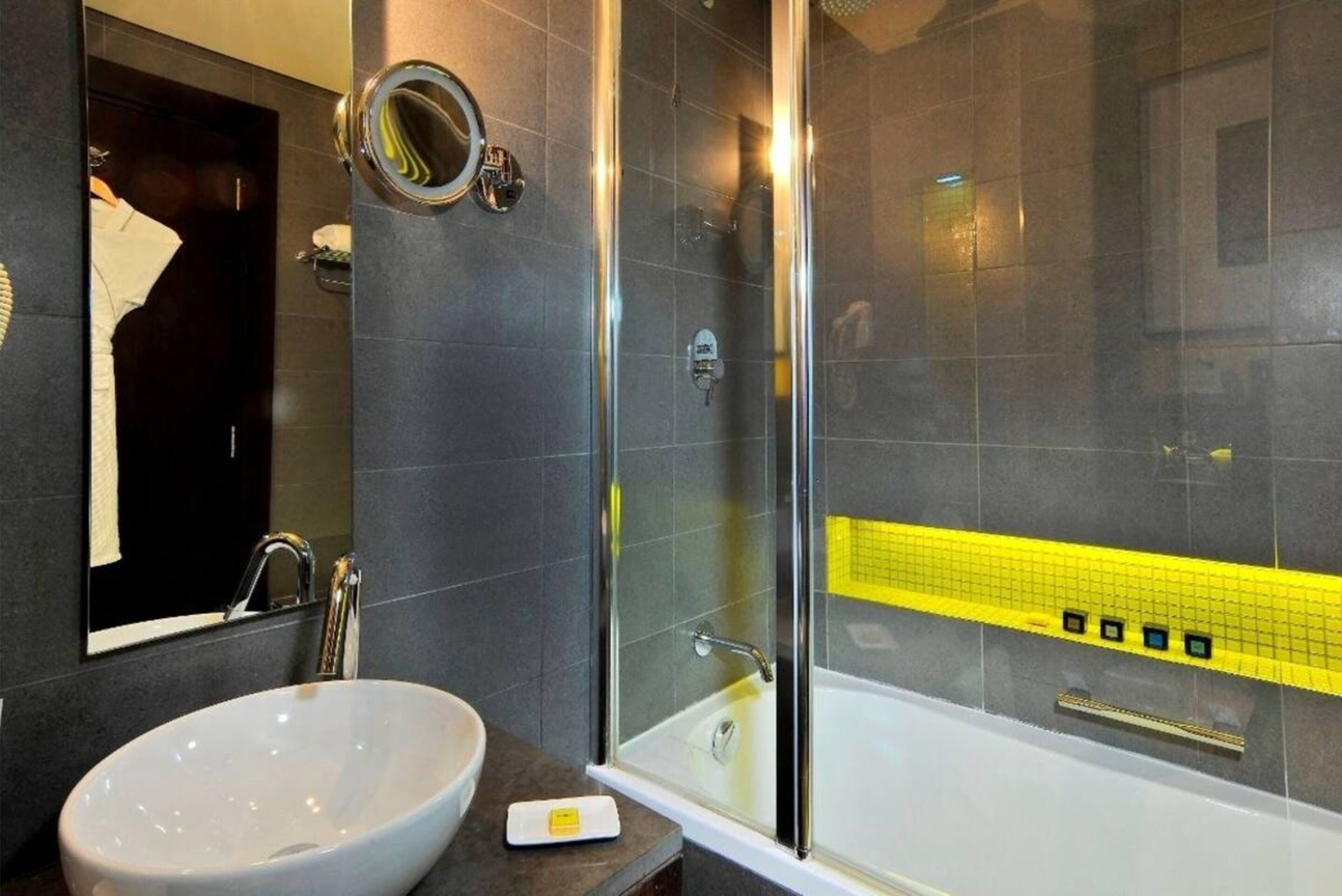 A modern bathroom with a white sink, a glass-enclosed shower, and a yellow-tiled shower area.