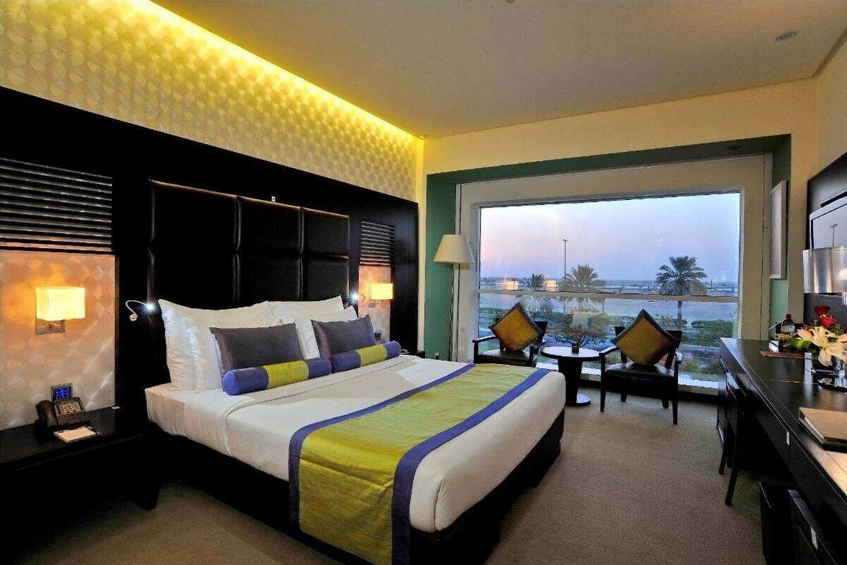 A hotel room with a large bed, two chairs, a desk, and a view of the cityscape.