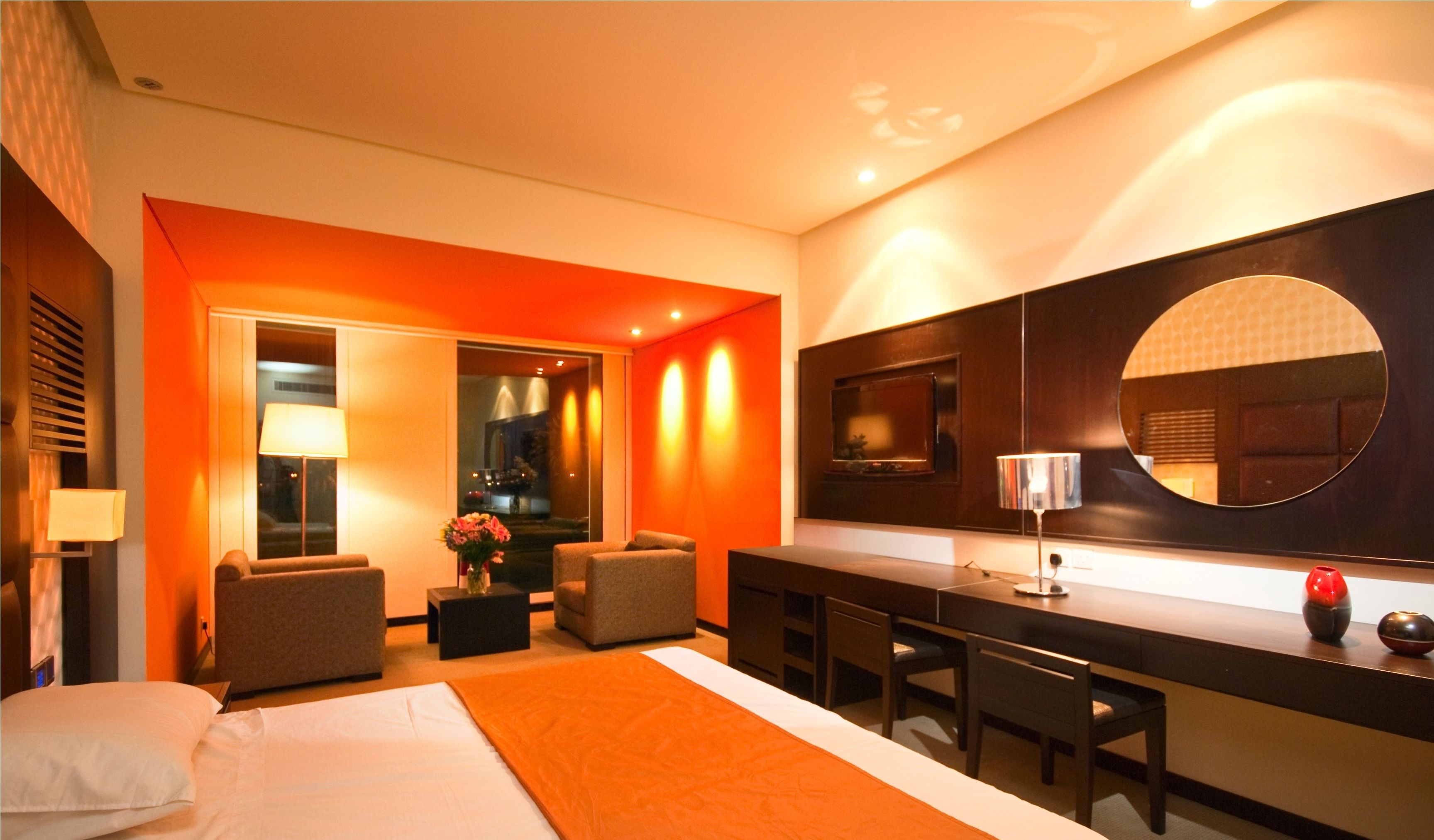 Une chambre d’hôtel moderne dotée d’un grand lit, d’un coin salon avec deux fauteuils, d’une petite table et d’un bar avec des tabourets.