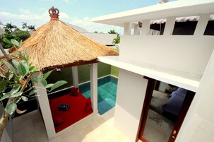 Uma villa moderna com telhado de palha, piscina e área de estar com assentos acolchoados vermelhos.