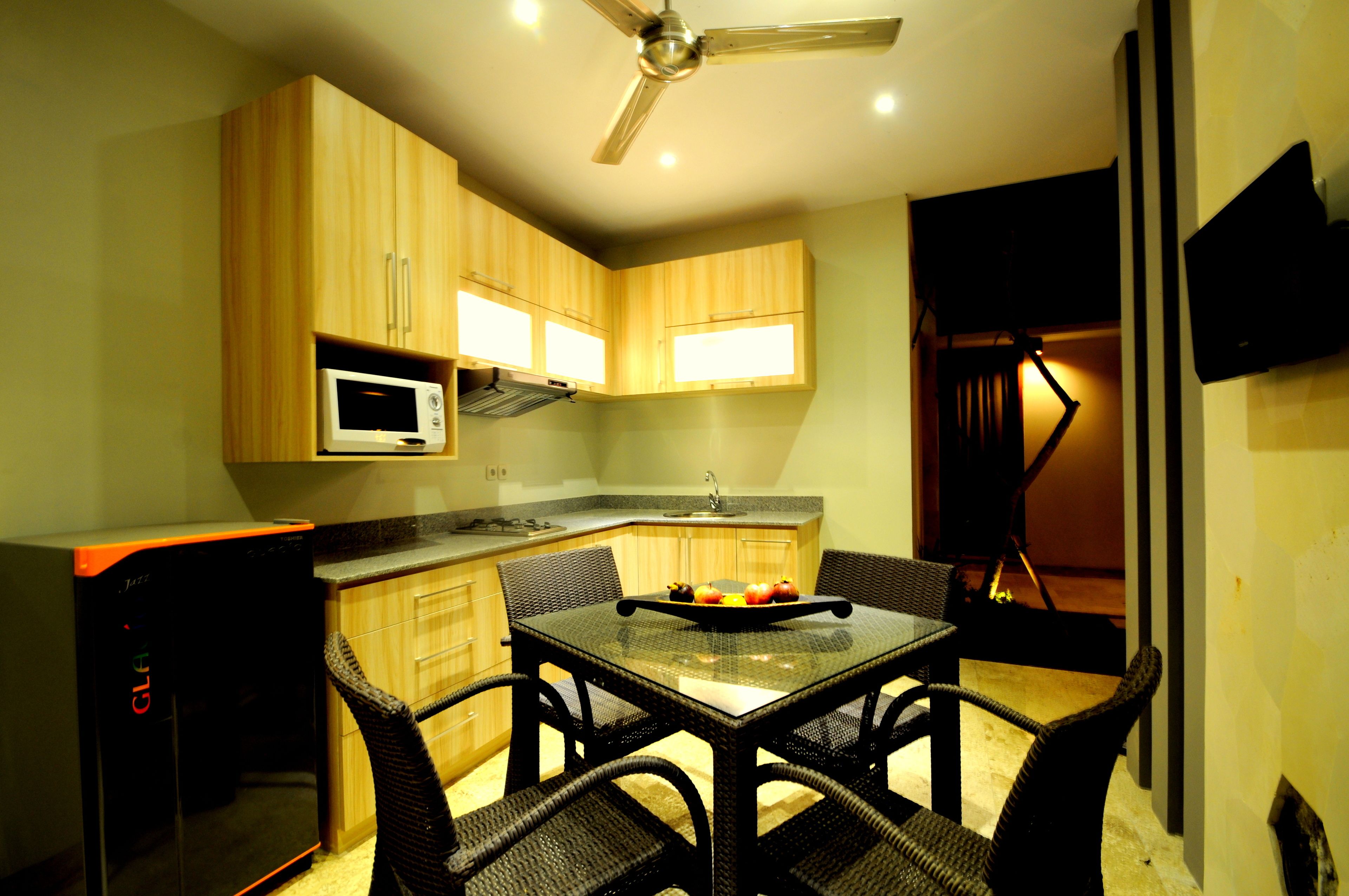 A compact kitchen with wooden cabinets, a microwave, a dining table with chairs, and a ceiling fan.