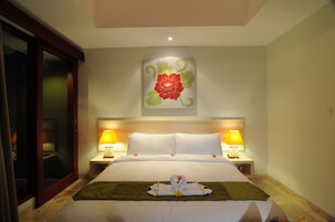 Quarto de hotel com uma cama, duas luminárias de cabeceira, uma obra de arte floral na parede e uma decoração de toalhas na cama.