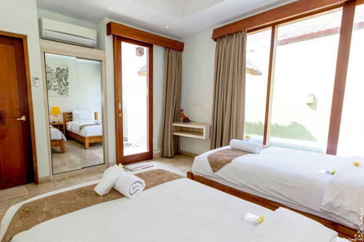 A hotel room with two beds, a desk, a mirror, and a door.