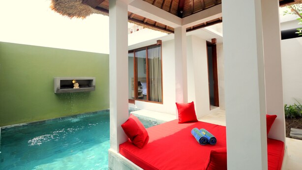 Zona piscina con una panca imbottita rossa, un tetto di paglia e un piccolo ripiano con un oggetto decorativo.