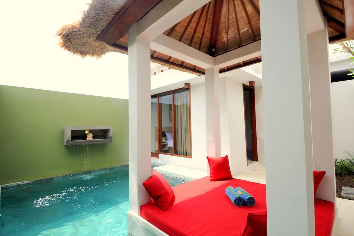 A poolside area with a red cushioned bench, a thatched roof, and a small shelf with a decorative item.