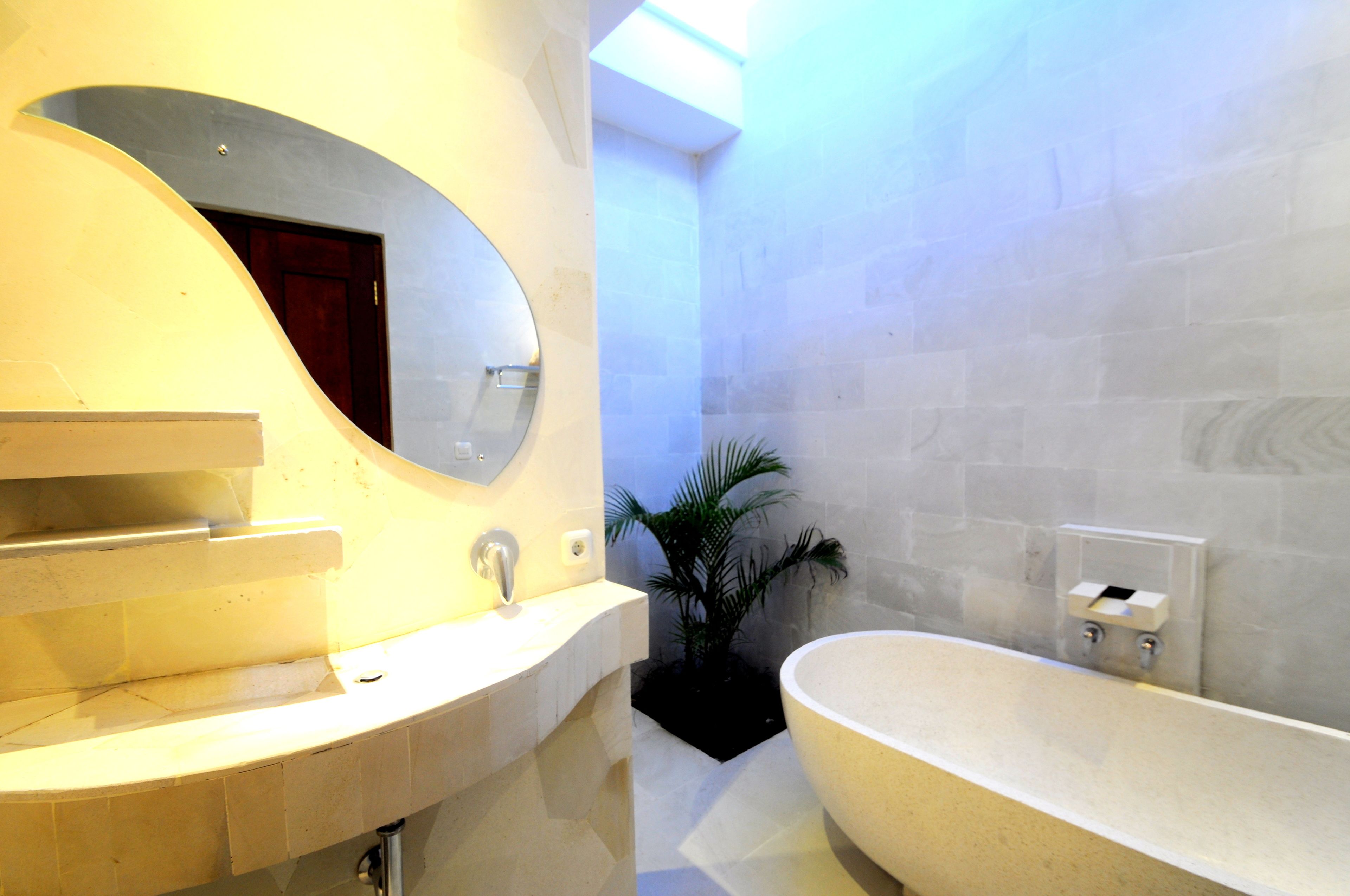 Et moderne badeværelse med et fritstående badekar, et stort spejl og en potteplante.